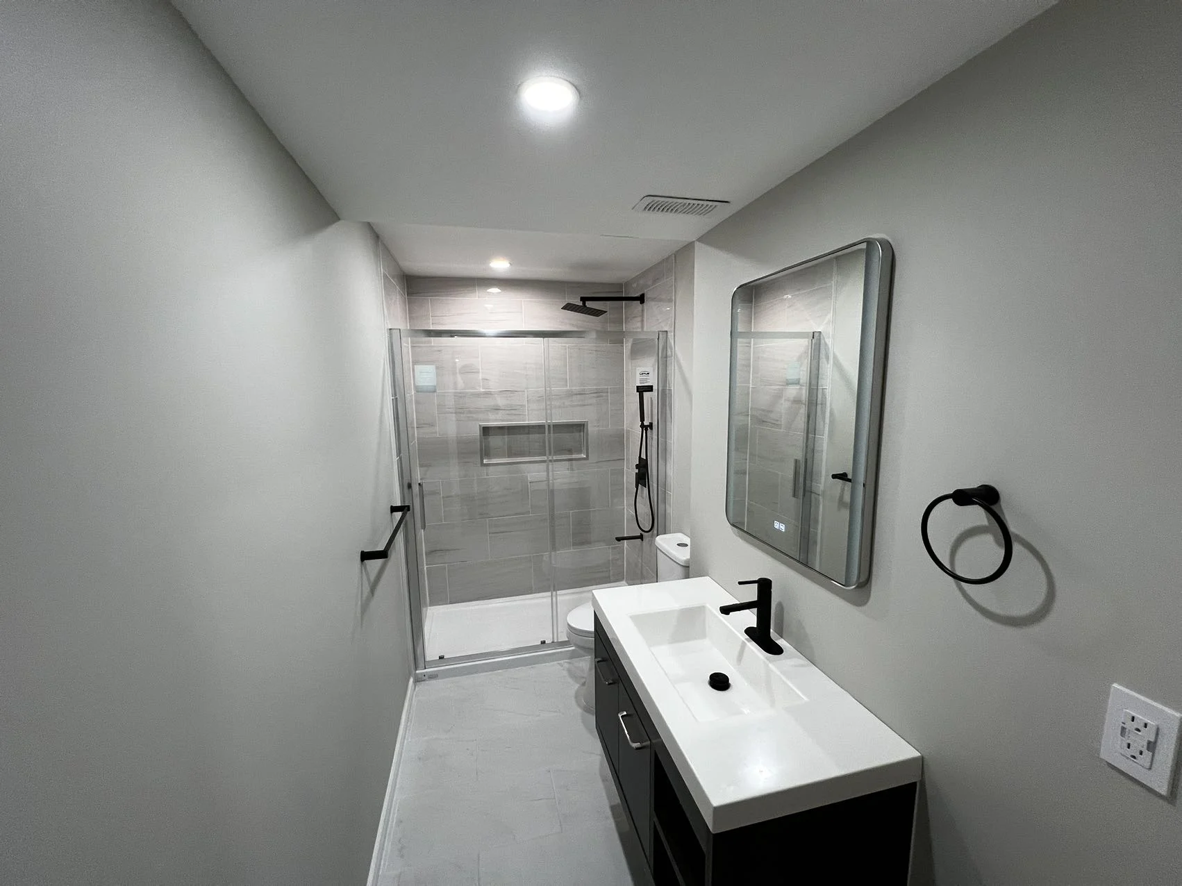 A narrow bathroom from Meiju’s project reference gallery, with glass-enclosed shower, recessed niche, single vanity and black fixtures.