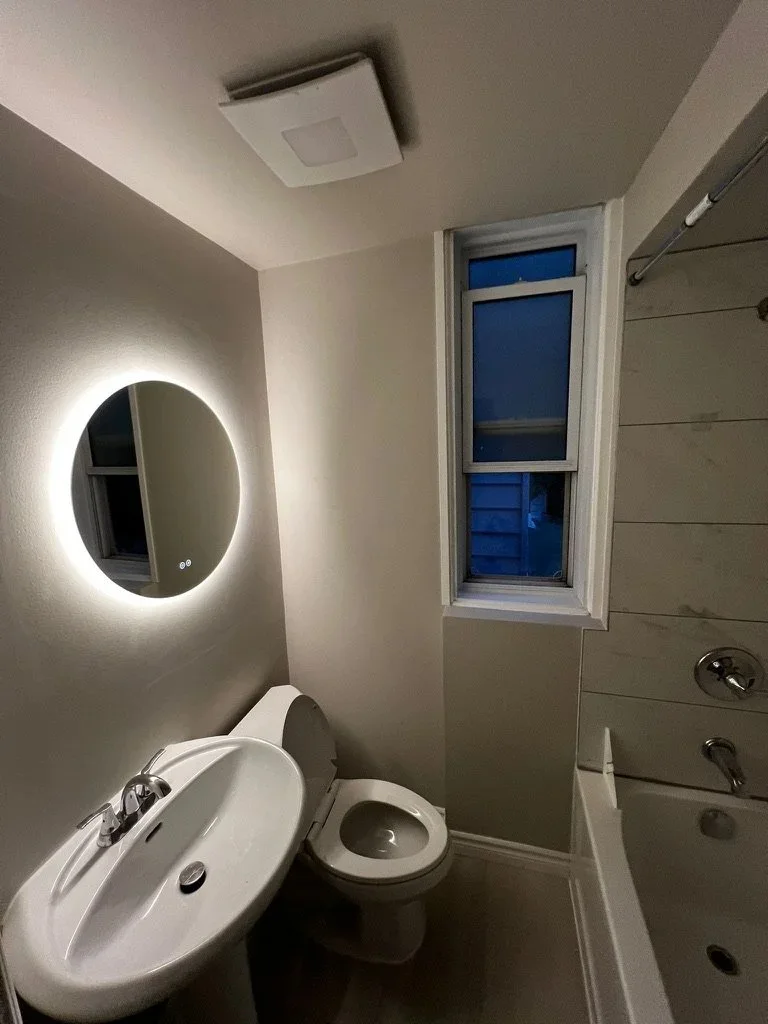 Compact Meiju bathroom with a pedestal sink, round illuminated mirror, toilet and adjacent bathtub.